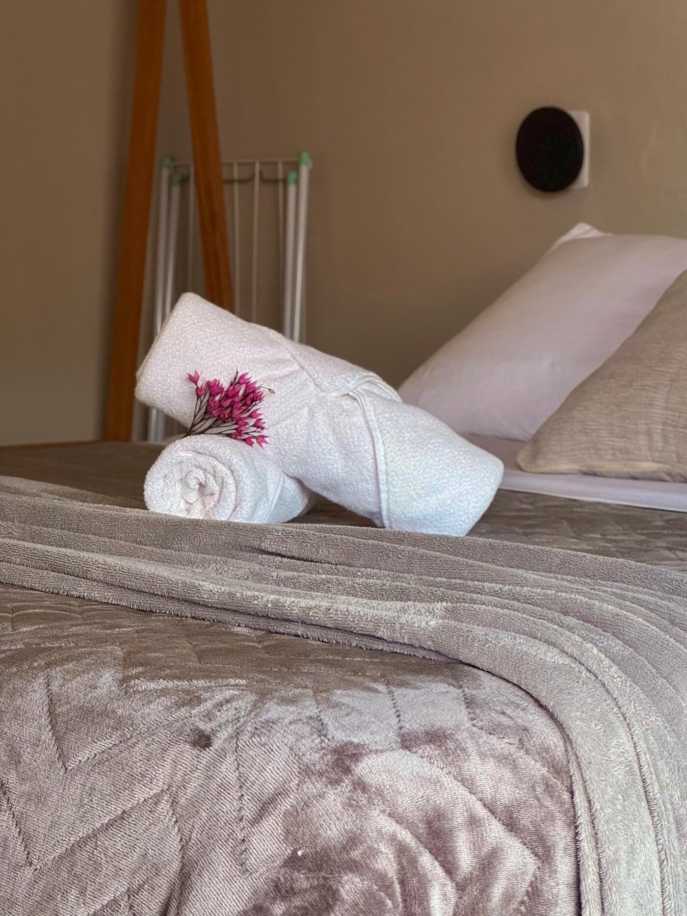 Cama arrumada com toalhas dobradas e flor sobre a manta